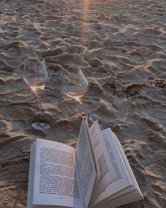 an open book and two wine glasses on the beach