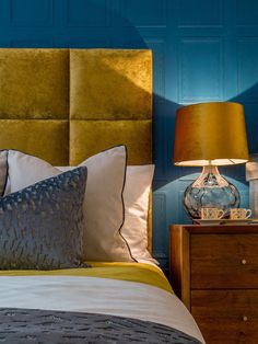 a bedroom with blue walls and gold headboard, two lamps on either side of the bed