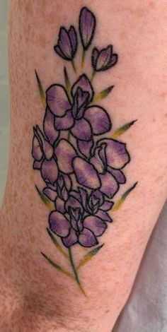 a close up of a person's leg with tattoos on it and purple flowers