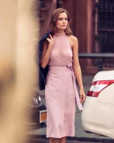 a woman in a pink dress is walking down the street with her hand on her hip