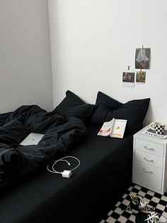 an unmade bed in a white room with checkered flooring and black sheets