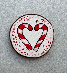 a red and white painted wooden slice with two candy canes in the shape of a heart