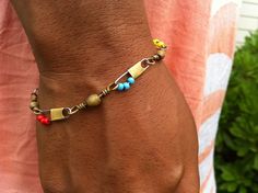 a man is wearing a bracelet with beads and charms on it's wrist while standing in front of a bush