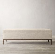 an upholstered bench with wooden legs in a white walled room, against a gray wall