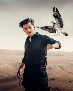 a man standing in the desert with an eagle on his shoulder and another bird flying above him