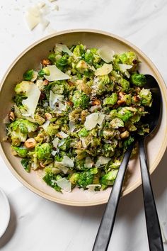 a bowl filled with chopped broccoli and other vegetables next to two spoons