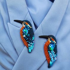 two colorful bird brooches are attached to a blue shirt with black pins on it