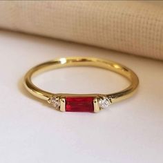 a gold ring with two diamonds and a red stone on the side, sitting on a white surface