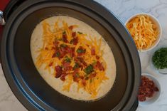 a crock pot filled with cheese and bacon on top of a table next to bowls of condiments