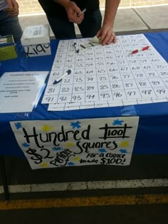 a man is writing numbers on a blue table with a sign that says hundred foot squares