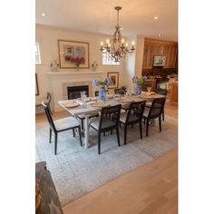 a dining room table with chairs and a chandelier hanging from the ceiling in front of a fireplace