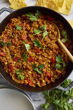 mexican rice in a skillet with tortilla chips and cilantro on the side