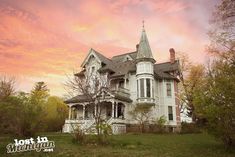 an old victorian style house sits in the middle of a grassy area with trees and bushes