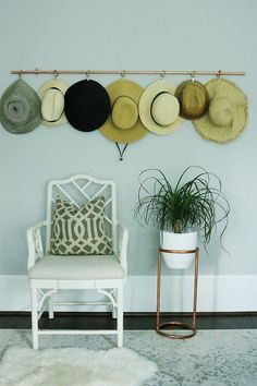 hats are hanging on the wall above a chair and potted plant in a room