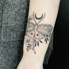 a moth tattoo on the left arm with flowers and crescent moon in it's center