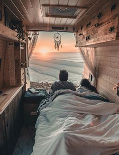 a person laying in bed looking out at the ocean from inside a truck with its door open