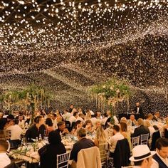 a large group of people sitting at tables in a room with lights on the ceiling