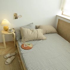 a bed with two pillows on top of it next to a night stand and lamp