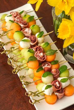 there are many fruits and veggies on skewers with flowers in the background