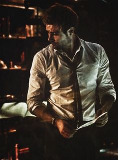 a man wearing a white shirt and tie standing in front of a book shelf filled with books