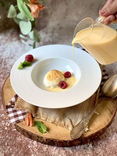 a person pouring milk onto a dessert on a plate with raspberries and cream