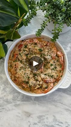 a white casserole dish with shrimp and parmesan cheese in it on a marble table