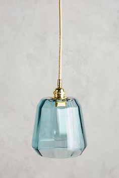 a blue glass light hanging from a gold colored metal hook on a white wall background