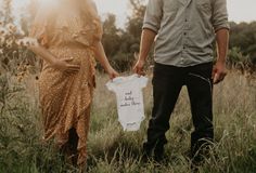 a man and woman standing next to each other in a field holding a t - shirt