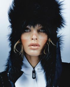 a woman with large hoop earrings and black fur on her head, wearing a jacket