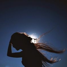 the silhouette of a woman with her hair blowing in the wind against a blue sky