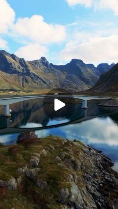 an aerial view of a bridge over a lake with mountains in the background and clouds in the sky