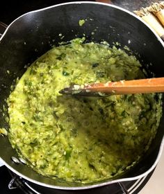 a pan filled with green food on top of a stove next to a wooden spatula