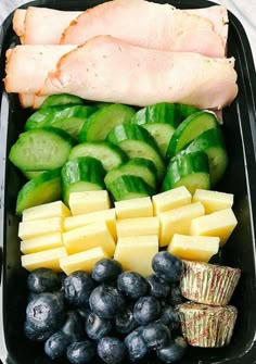 a black container filled with lots of different types of food next to blueberries and cucumbers