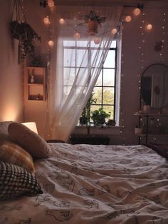 a bed sitting under a window next to a night stand with lights hanging from it