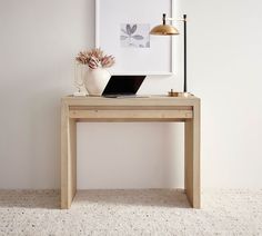 a wooden table with a laptop on it in front of a white wall and lamp