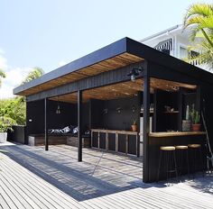 an outdoor bar with stools and tables on a deck next to palm trees in front of a house