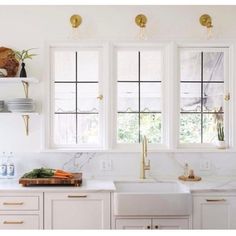 a white kitchen with marble counter tops and gold trim on the windows above the sink