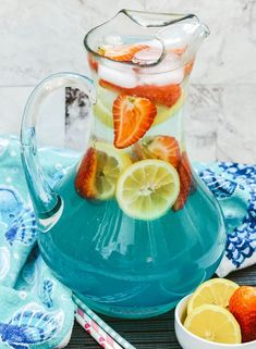 a pitcher filled with lemons, strawberries and water next to a bowl of fruit