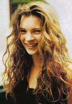 a close up of a person with long hair smiling and wearing a black shirt,