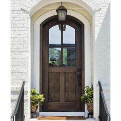 the front door to a white brick house with two potted plants on either side