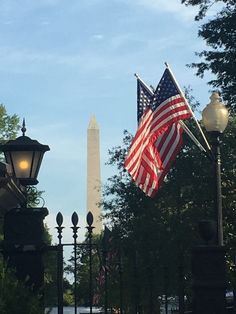 an american flag flying in front of the washington monument with street lamps on either side