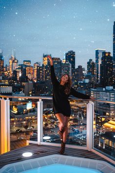 a woman standing on top of a balcony in front of a cityscape at night