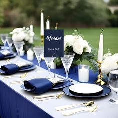 a table set with blue and white place settings, silverware, candles, and napkins