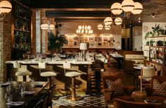 an empty restaurant with tables and chairs in front of the bar, lights hanging from the ceiling