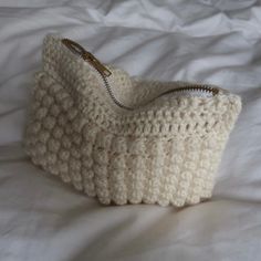 a white crocheted purse sitting on top of a bed next to a pillow