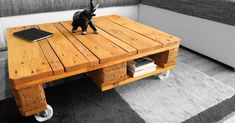 a wooden coffee table with wheels and a cat figurine sitting on top of it