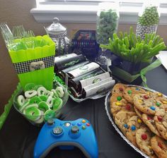 a table topped with cookies, candy and other items next to a video game controller