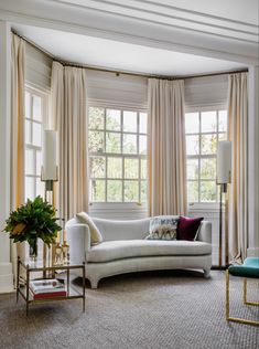 a living room filled with furniture next to two large windows covered in white drapes