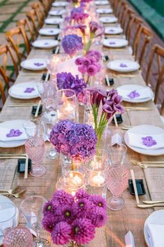 a long table is set with purple flowers and candles for an elegant dinner or party