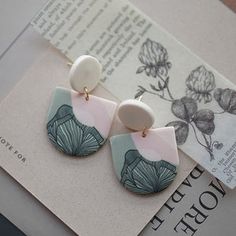 a pair of earrings sitting on top of a piece of paper next to a book